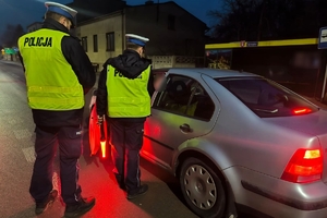 Zdjęcie przedstawia dwóch policjantów kontrolujących trzeźwość kierowcy.