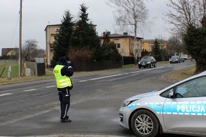 Zdjęcie przedstawia policjanta z urządzeniem pomiarowym oraz pojazdy.