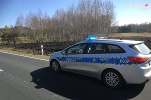 radiowóz stoi przy polu, na którym wypalono trawę