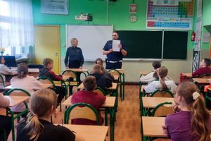 Zdjęcie przedstawia policjantów oraz dzieci w sali przy ławkach.