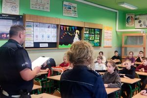 Zdjęcie przedstawia policjantów oraz dzieci w sali przy ławkach.