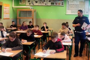 Zdjęcie przedstawia policjanta oraz dzieci w sali przy ławkach.