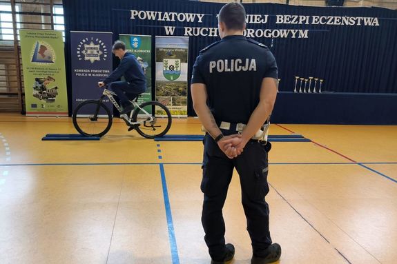 Zdjęcie przedstawia policjanta oraz chłopaka na rowerze w sali gimnastycznej.