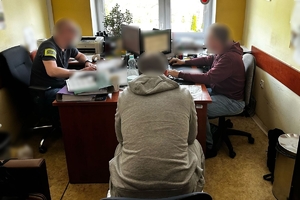 Zdjęcie przedstawia policjantów i zatrzymanego w pomieszczeniu podczas przesłuchania.
