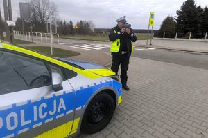 Zdjęcie przedstawia policjanta z radarem oraz radiowóz.