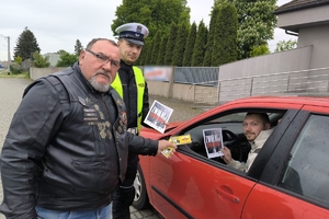 Zdjęcie przedstawia policjanta oraz motocyklistę przekazujących naklejkę kierowcy.