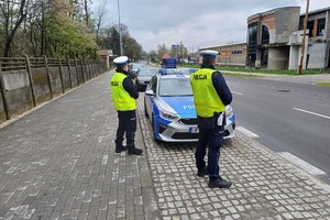 Zdjęcie przedstawia dwóch policjantów oraz radiowóz.