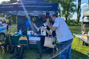 Zdjęcie przedstawia mężczyznę z aparatem fotograficznym obok stoiska policyjnego.