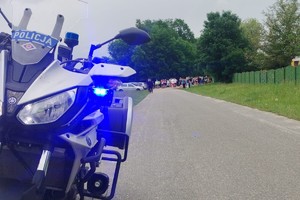 Zdjęcie przedstawia policyjny motocykl oraz uczestników biegu.
