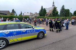 Zdjęcie przedstawia policjanta, strażaków, uczestników rajdu oraz policyjny radiowóz.