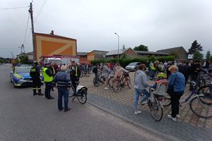 Zdjęcie przedstawia policjanta, strażaków, uczestników rajdu oraz policyjny radiowóz.