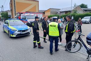 Zdjęcie przedstawia policjanta, strażaków, uczestników rajdu oraz policyjny radiowóz.