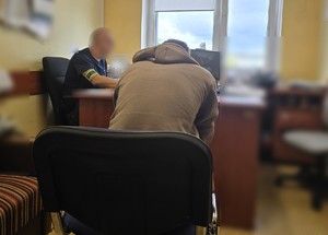 Zdjęcie przedstawia nieumundurowanego policjanta oraz mężczyznę w policyjnym pomieszczeniu.