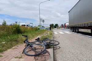 policjanci wykonują czynności na miejscu zdarzenia drogowego, na zdjęciu widać samochód ciężarowy oraz uszkodzony rower oraz oznakowane radiowozy