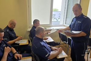Zdjęcie przedstawia policjanta rozdającego arkusze innym policjantom.