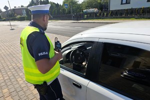 policjant stoi przy białym samochodzie, w ręce trzyma miernik prędkości