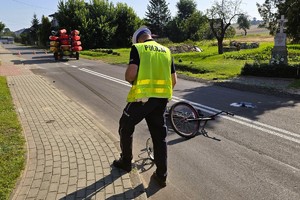 policjant prowadzi oględziny na miejscu wypadku, na zdjęciu widać rower i pojazd biorące udział w zdarzeniu
