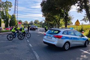 uczniowie w kamizelkach odbalskowych jadą na rowerach, drogę zabezpiecza radiowóz