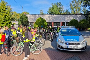 uczniowie na rowerach pozują do zdjęcia, obok stoi radiowóz oraz umundurowana policjantka
