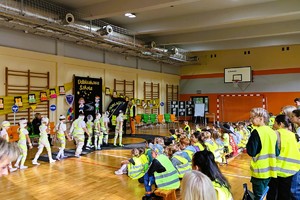 na zdjęciu umundurowane policjant i dzieci w odblaskowych kamizelkach, działania na sali sportowej