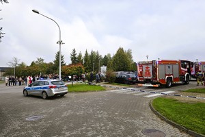 Na zdjęciu miejsce działań służb ratunkowych – radiowóz policyjny i wozy straży pożarnej na parkingu przy budynkach mieszkalnych.