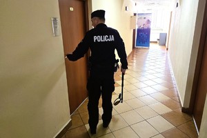 Na zdjęciu policjant idzie korytarzem budynku, kierując się w stronę drzwi. Korytarz jest dobrze oświetlony.