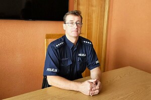 Dzielnicowy Adam Chudziński w mundurze służbowym, siedzi za biurkiem