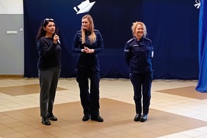 Trzy kobiety stoją przed publicznością w sali szkolnej, dwie z nich w mundurach policyjnych.