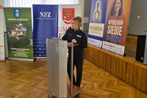 Policjantka prowadzi wystąpienie przy mównicy na tle banerów kampanii „Moc Decyzji”.
