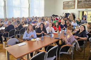 Uczestnicy konferencji siedzą przy stołach i słuchają prelegentów.