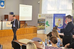 Prelegent występuje przed uczestnikami, obok ekran z prezentacją.