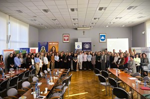 Grupa uczestników konferencji stoi wspólnie do zdjęcia na tle banerów profilaktycznych.