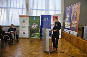 Policjantka prowadzi wystąpienie przy mównicy na tle banerów kampanii „Moc Decyzji”.