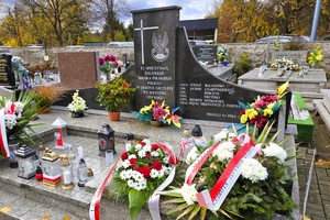 Zbiorowa mogiła żołnierzy udekorowana kwiatami i zniczami.