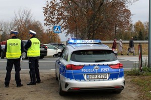 dwóch umundurowanych policjantów stoi przy radiowozie