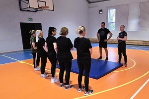 panie biorące udział w ćwiczeniach stoją na sali gimnastycznej wraz z dwoma instruktorami