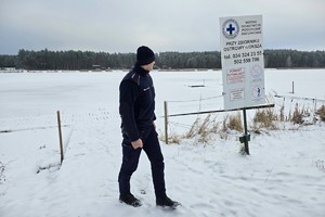 umundurowany dzielnicowy idzie przy zamarzniętym zbiorniku wodnym