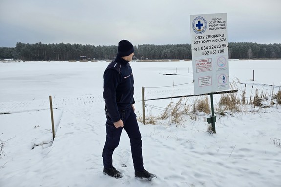 umundurowany dzielnicowy idzie przy zamarzniętym zbiorniku wodnym