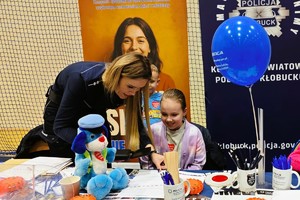 na stoisku policyjnym policjantka pokazuje kolorowankę dziecku