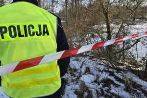 policjant umundurowany, stoi tyłem przy taśmie zabezpieczającej miejsce zdarzenia, zamarznięty zbiornik wodny