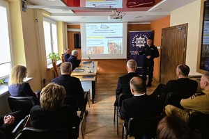Odprawa służbowa policjantów, na zdjęciu widać grupę umundurowanych policjantów oraz kobiety i mężczyzn ubranych po cywilnemu, w tle rzutnik, na którym prezentowane są treści dotyczące bezpieczeństwa powiatu kłobuckiego