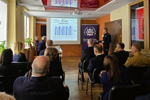 Odprawa służbowa policjantów, na zdjęciu widać grupę umundurowanych policjantów oraz kobiety i mężczyzn ubranych po cywilnemu, w tle rzutnik, na którym prezentowane są treści dotyczące bezpieczeństwa powiatu kłobuckiego
