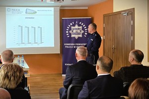 Odprawa służbowa policjantów, na zdjęciu widać grupę umundurowanych policjantów oraz kobiety i mężczyzn ubranych po cywilnemu, w tle rzutnik, na którym prezentowane są treści dotyczące bezpieczeństwa powiatu kłobuckiego