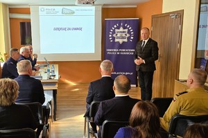 Odprawa służbowa policjantów, na zdjęciu widać grupę umundurowanych policjantów oraz kobiety i mężczyzn ubranych po cywilnemu, w tle rzutnik, na którym prezentowane są treści dotyczące bezpieczeństwa powiatu kłobuckiego