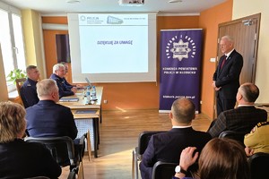 Odprawa służbowa policjantów, na zdjęciu widać grupę umundurowanych policjantów oraz kobiety i mężczyzn ubranych po cywilnemu, w tle rzutnik, na którym prezentowane są treści dotyczące bezpieczeństwa powiatu kłobuckiego