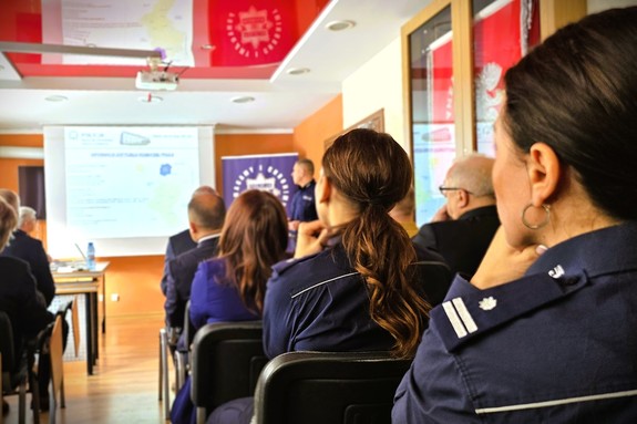 Odprawa służbowa policjantów, na zdjęciu widać grupę umundurowanych policjantów oraz kobiety i mężczyzn ubranych po cywilnemu, w tle rzutnik, na którym prezentowane są treści dotyczące bezpieczeństwa powiatu kłobuckiego