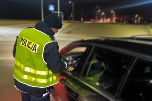 umundurowany policjant bada trzeźwość kierowcy, który siedzi w samochodzie
