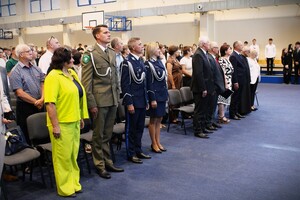 uroczystość rozpoczęcia roku szkolnego, na sali gimnastycznej stoją uczniowie, nauczyciele oraz zaproszeni goście