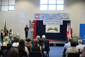 uroczystość rozpoczęcia roku szkolnego, na sali gimnastycznej stoją uczniowie, nauczyciele oraz zaproszeni goście